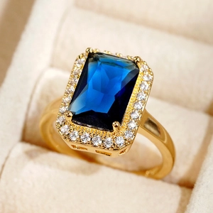 Macro shot of gold ring featuring a large rectangular blue gemstone with diamond halo