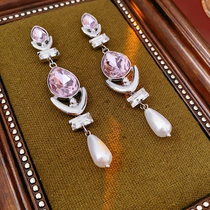 Close-up of vintage earrings with pink crystals and teardrop pearls on green velvet