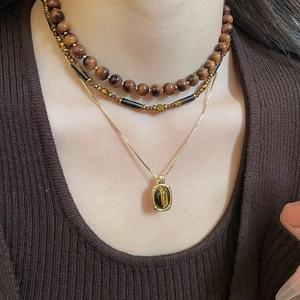 Detail of layered tiger eye beaded necklaces with golden pendants on a brown sweater