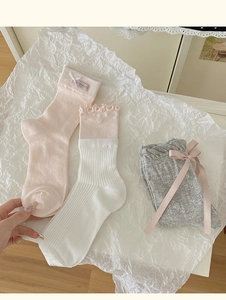 Dettaglio calzini con fiocco rosa e calze in pizzo su sfondo di carta bianca