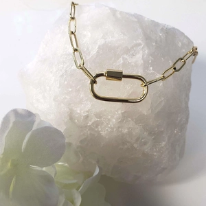 Gold stainless steel carabiner clasp necklace displayed on white crystal stone with flowers