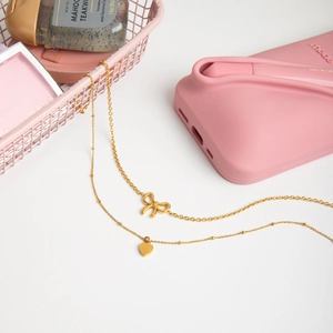 Detail of 18K gold stainless steel layered necklaces with bow and heart pendants