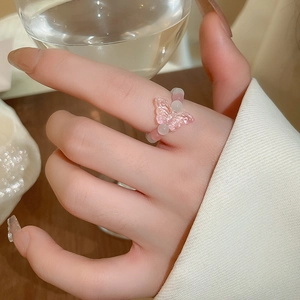 Detail of a pink glass butterfly beaded elastic ring worn by a model holding a glass cup