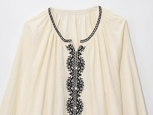 Close-up of black geometric embroidery and buttons on a cream cotton linen blouse