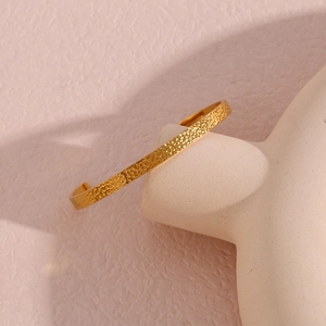 Macro detail of 18K gold plated bangle showing unique hammered texture on ceramic stand