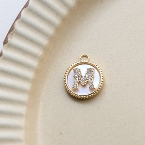 Macro shot of 18k gold plated round pendant with pearl inlay and CZ letter M