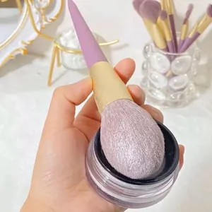 Purple makeup brush with tapered handle and golden ferrule applying loose powder
