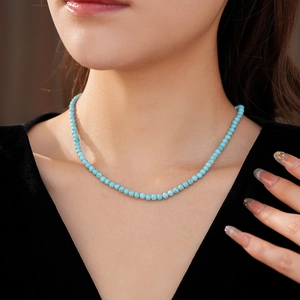 Close-up of minimalist turquoise beaded necklace worn by a model in soft lighting