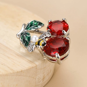 Close-up of crystal cherry brooch featuring red gemstones and a small pearl bee detail
