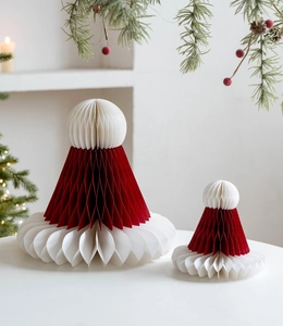 Détail d'ornements en papier alvéolé rouge et blanc sur fond festif de branches de pin