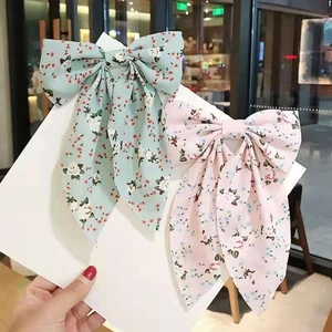 Floral bow hair clips in pink and green with long ribbons shown on a display card