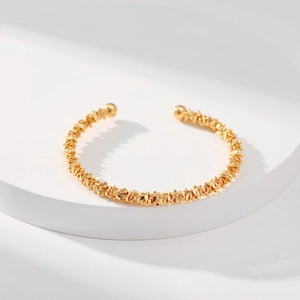 Detalle del brazalete dorado con textura irregular y extremos de bolas metálicas redondas