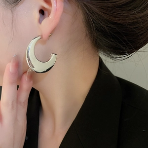 Close-up of polished silver C-shaped metal hoop earrings worn by a model