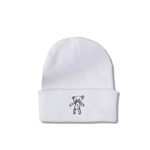 Détail d'un bonnet en maille blanche avec broderie d'ours noir sur le revers plié