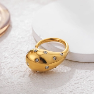 Macro detail of gold-plated teardrop ring with pavé zircons on white stone texture