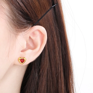 Vue macro de boucles d'oreilles cœur dorées avec pierre rouge portée à l'oreille