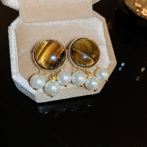 Dettaglio di orecchini vintage occhio di tigre con montatura dorata e nappine di perle