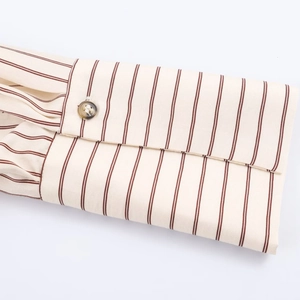 Detalle del puño de camisa a rayas beige con costuras finas y botón de resina