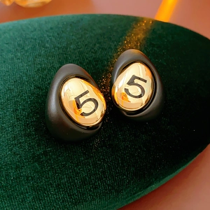 Detailed macro view of black and gold drop earrings featuring a numeral 5 design
