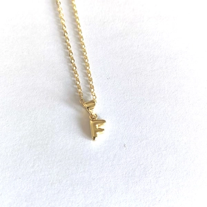 Detailed macro view of minimalist gold letter F pendant necklace on white surface