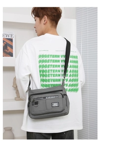 Detailed side view of multi-pocket grey canvas crossbody bag worn by a male model