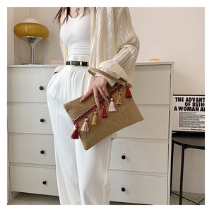 Detail of hand-woven straw envelope clutch bag with colorful tassels and linen texture