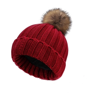 Detail of red cable knit beanie featuring thick texture and brown faux fur pom pom