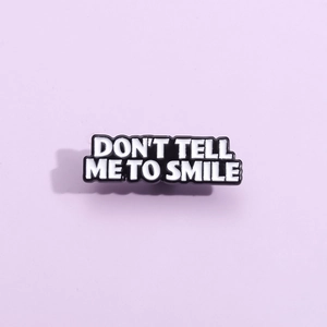 Creative black enamel pin featuring Don't Tell Me To Smile text on purple background