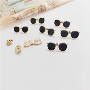 Macro view of sunglasses enamel pins showing golden frames and metal butterfly clutches