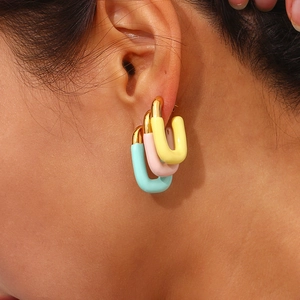 Close-up of U-shaped gold earrings in mint green, light pink, and bright yellow on model