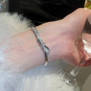 Close-up of a silver bow-knot bracelet with pavé rhinestones worn by a model