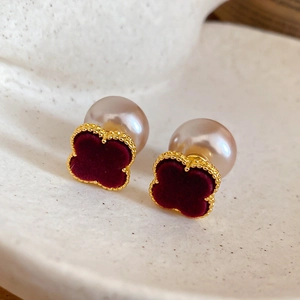Detail of red velvet clover earrings with gold frame and small pearls on a ceramic dish