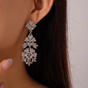 Dettaglio di orecchini a fiore metallici traforati con motivi stratificati per donna