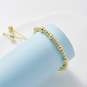 Detail of adjustable gold beaded bracelet on light blue pedestal with smooth metal texture