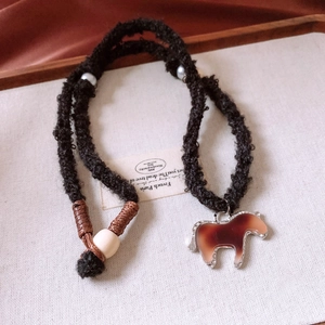 Close-up of woven rope necklace with red resin horse pendant and decorative white bead