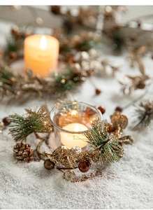 Détail d'une couronne de Noël avec pommes de pin dorées, boule et bougie dans un photophore