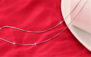 Close-up of 1mm silver plated snake chain necklaces on red fabric with bright highlights