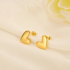 Detail of 18k gold plated heart studs on a soft beige silk fabric background