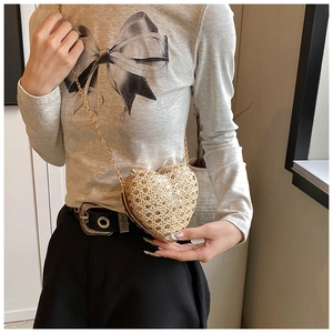 Chic gold heart-shaped clutch bag with rhinestones and long chain strap held by a model