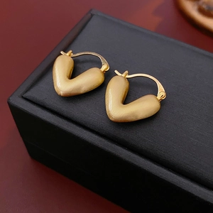 Macro detail of V-shaped gold hoop earrings with a matte brushed metallic finish