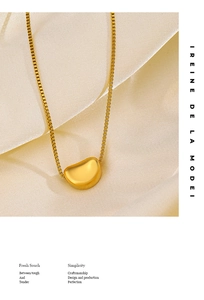 Detailed view of a golden bean pendant on a box chain over elegant silk fabric