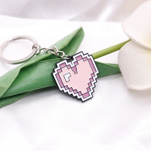 Close-up of pink pixel heart keychain on white silk background with floral accents