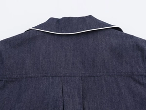 Detail of dark blue denim shirt with white piping and back pleat on white background