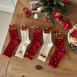 Detail of red and cream Christmas socks with bows and floral embroidery on wood
