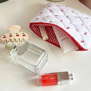 Detail of quilted white cosmetic bag with red cherry prints and matching hair claw clip