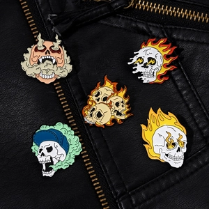 Close-up of five gothic skull enamel pins with flames and lightning on a black leather jacket