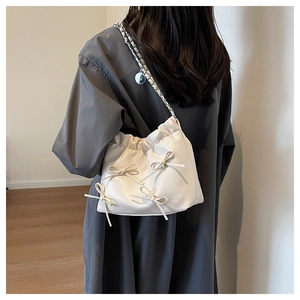 Side view of ivory faux leather shoulder bag with decorative bows and silver chain strap