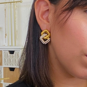 Close-up of interlocking gold and pearl double diamond earrings on a model's ear