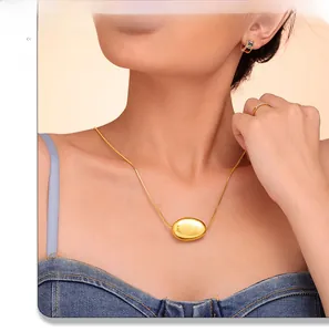Close-up of polished gold-plated bean pendant on a layered snake chain necklace worn by model
