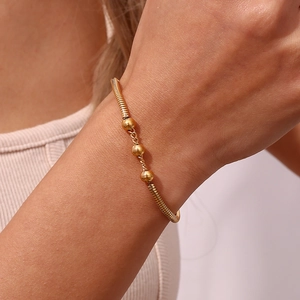 Macro shot of gold snake chain bracelet with three golden beads on woman's wrist